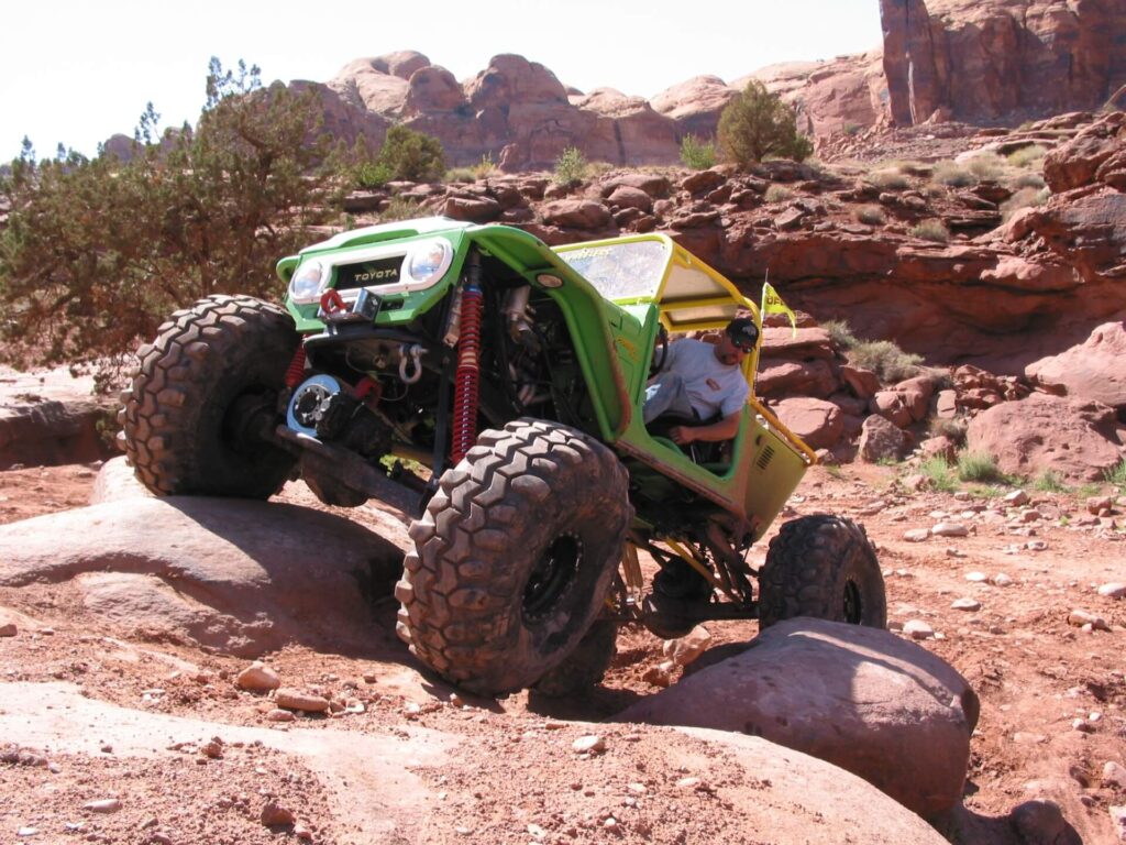 A toyota land cruiser FJ45 in green with large wheels rolling over rocks